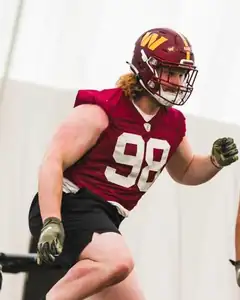 Adam Raine mid-stride in a helmet and a burgundy Washington Commanders practice jersey at an indoor practice field.
